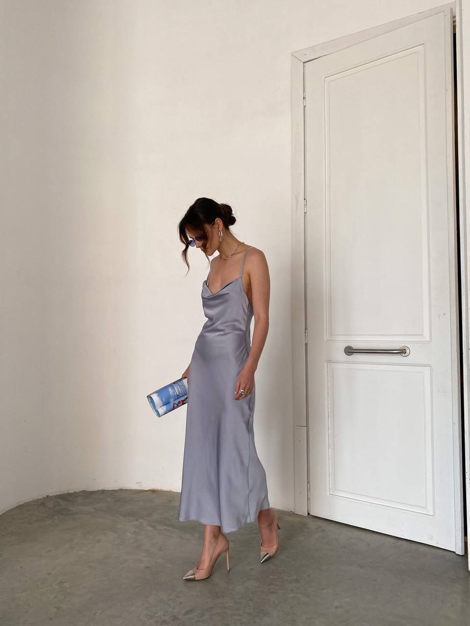 Woman in a gray dress standing in a minimalistic room with a white door.