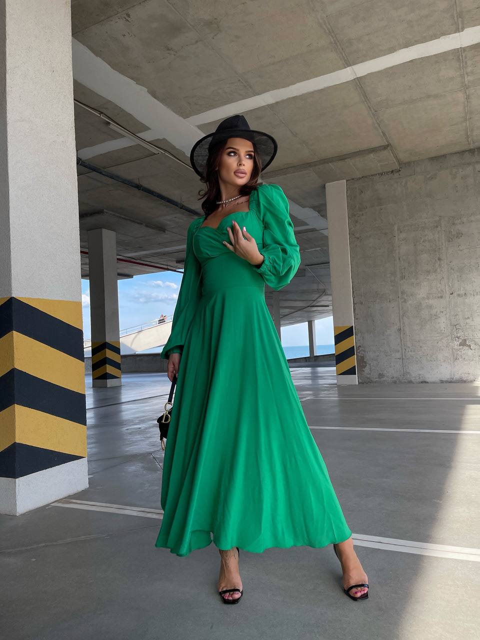 Woman in a green dress and black hat standing in an underpass.