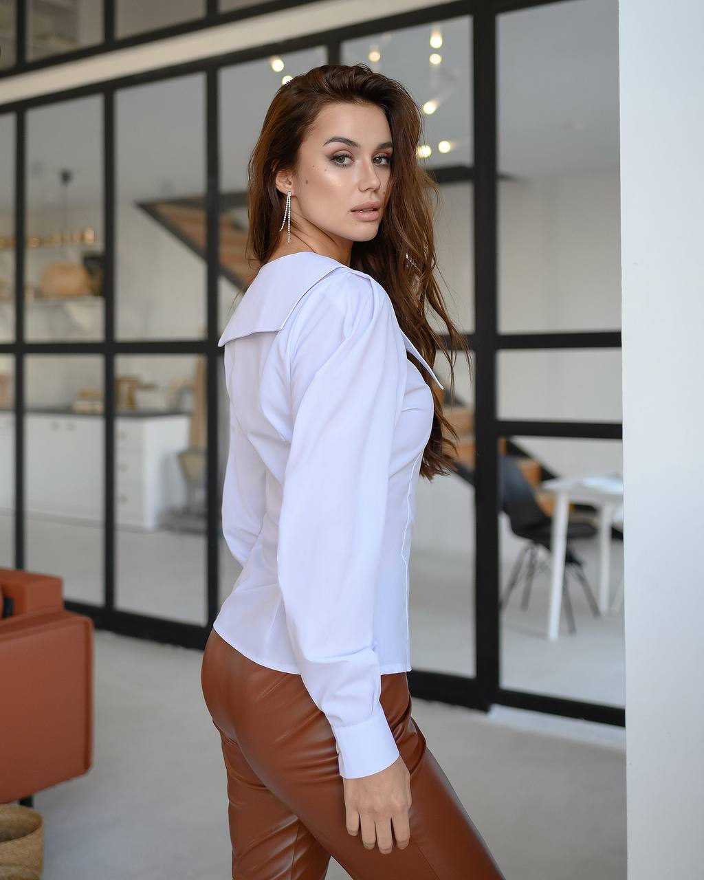 Woman wearing a white blouse and brown pants in an indoor setting