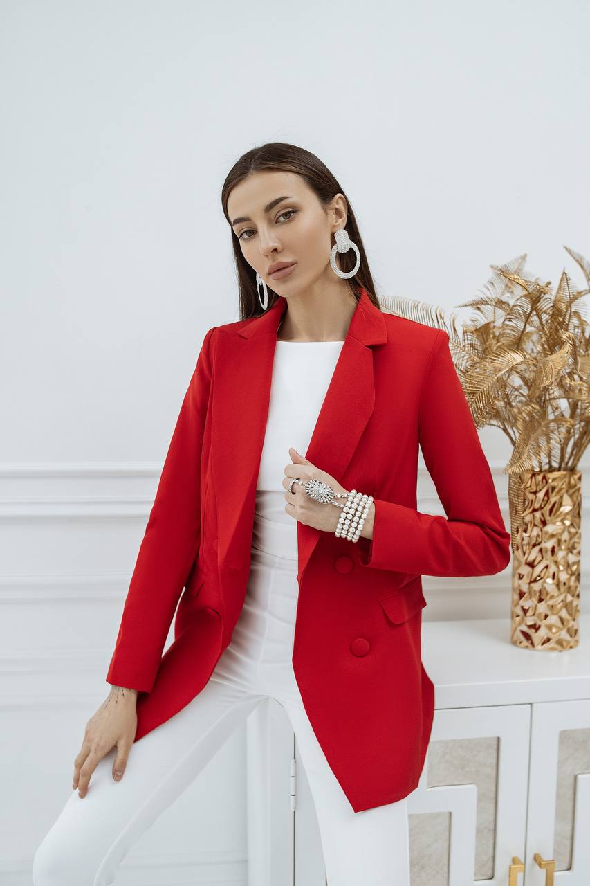Woman wearing a red blazer over a white outfit in a minimalistic setting.