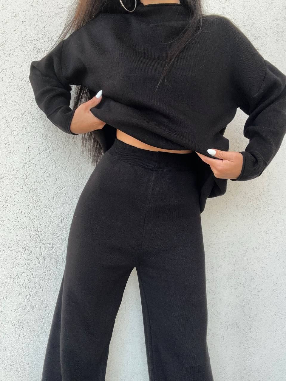 Person wearing a black cropped hoodie and black pants against a light gray background