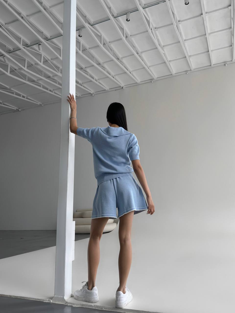 Person wearing a light blue outfit standing in a minimalistic room.