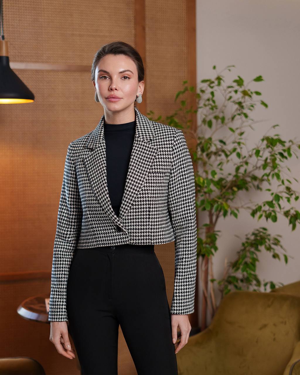 Woman wearing a checkered blazer over a black top in an indoor setting with plants.