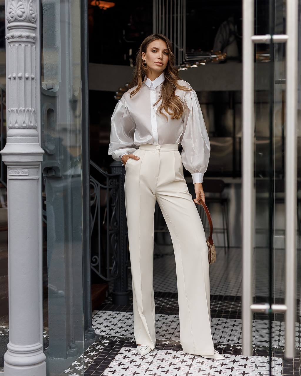Woman in a white outfit standing in front of a glass door.
