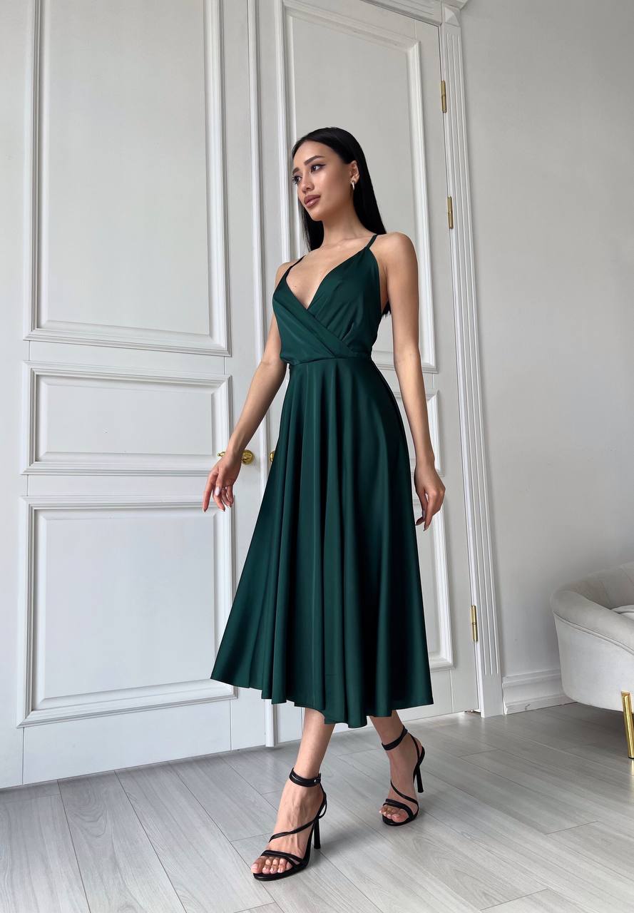 Woman wearing a green dress standing in a room with white walls and a door.