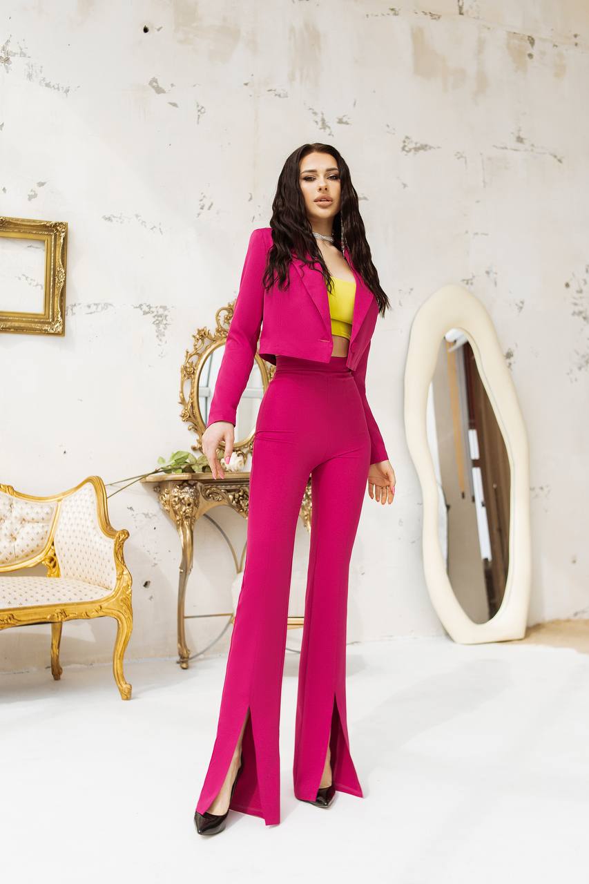 Woman in a bright pink outfit standing in an elegant room with gold furniture and a white wall.