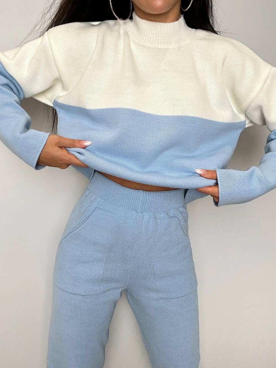 Two-tone sweater with white and light blue colors worn by a person on a plain background