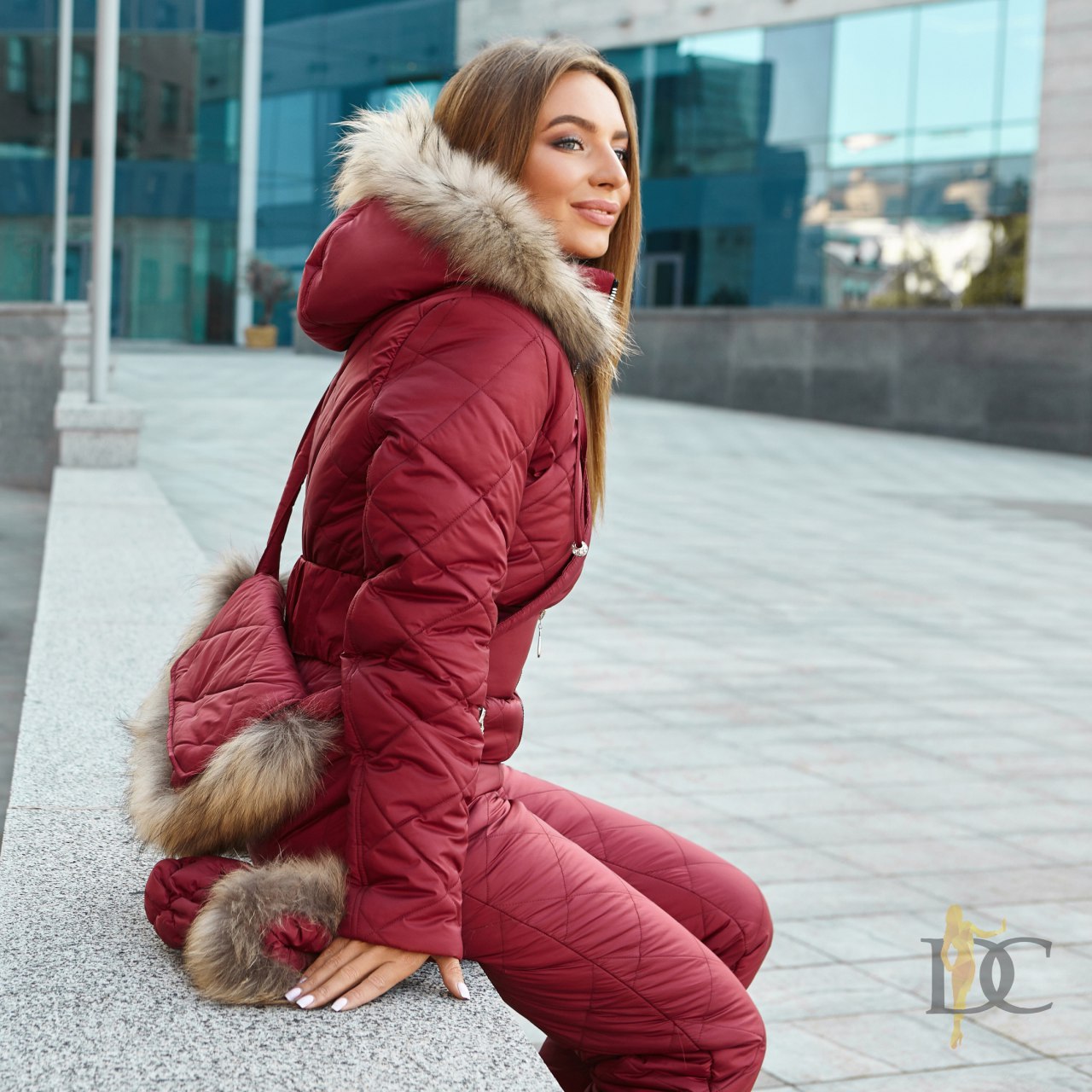 Woman in a red winter coat with fur hood and cuffs standing on a city street.