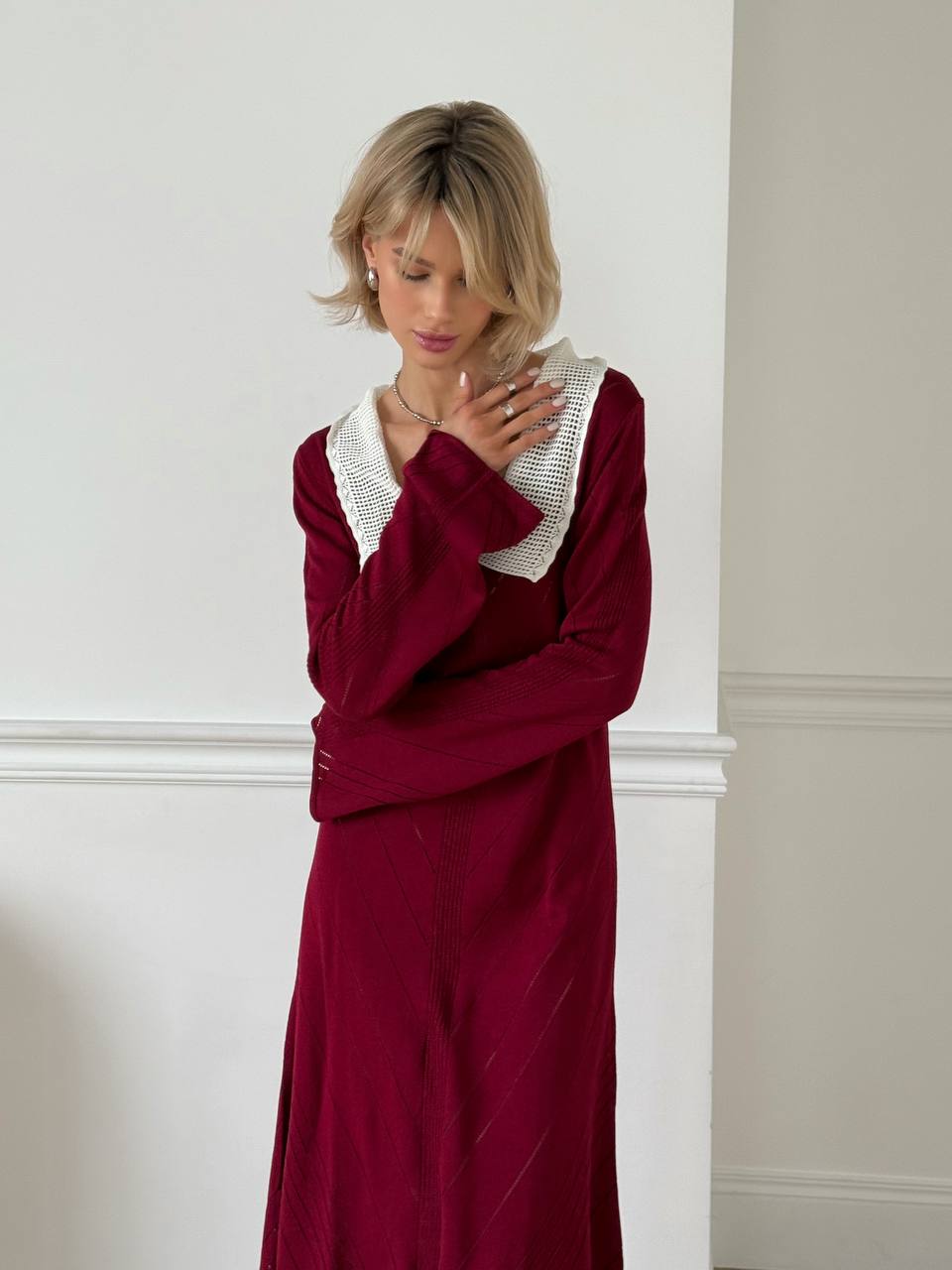 Woman wearing a burgundy dress with a white collar against a white wall