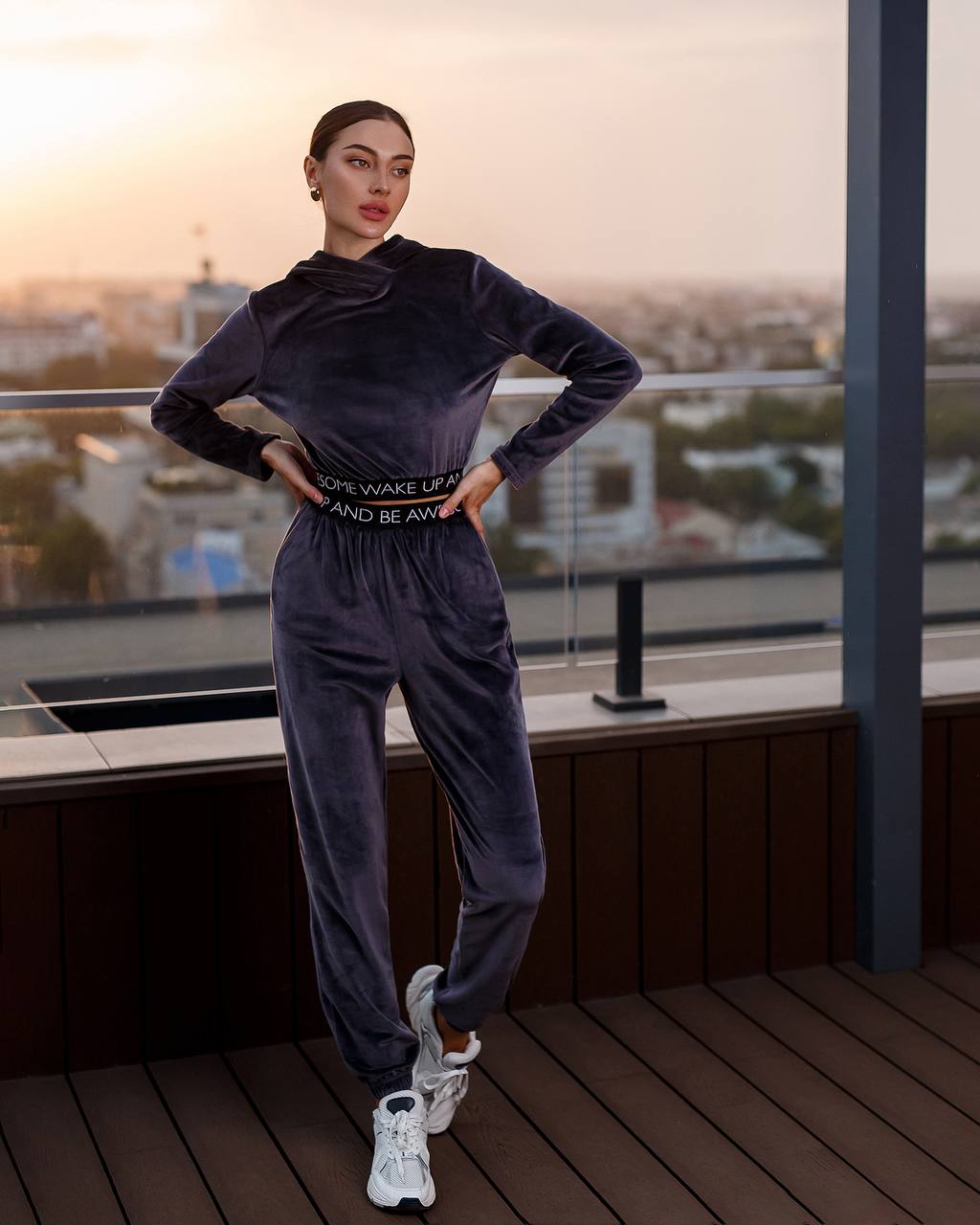 Woman in a dark tracksuit standing on a rooftop with a cityscape in the background