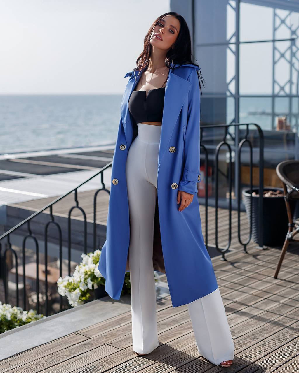 Woman wearing a blue coat standing on a wooden deck with ocean view