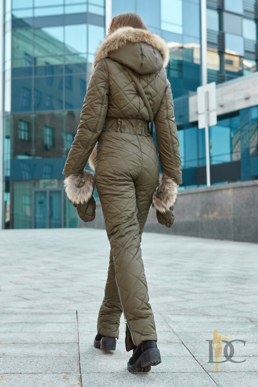 Person wearing a green puffer suit with fur trim walking on a city street.