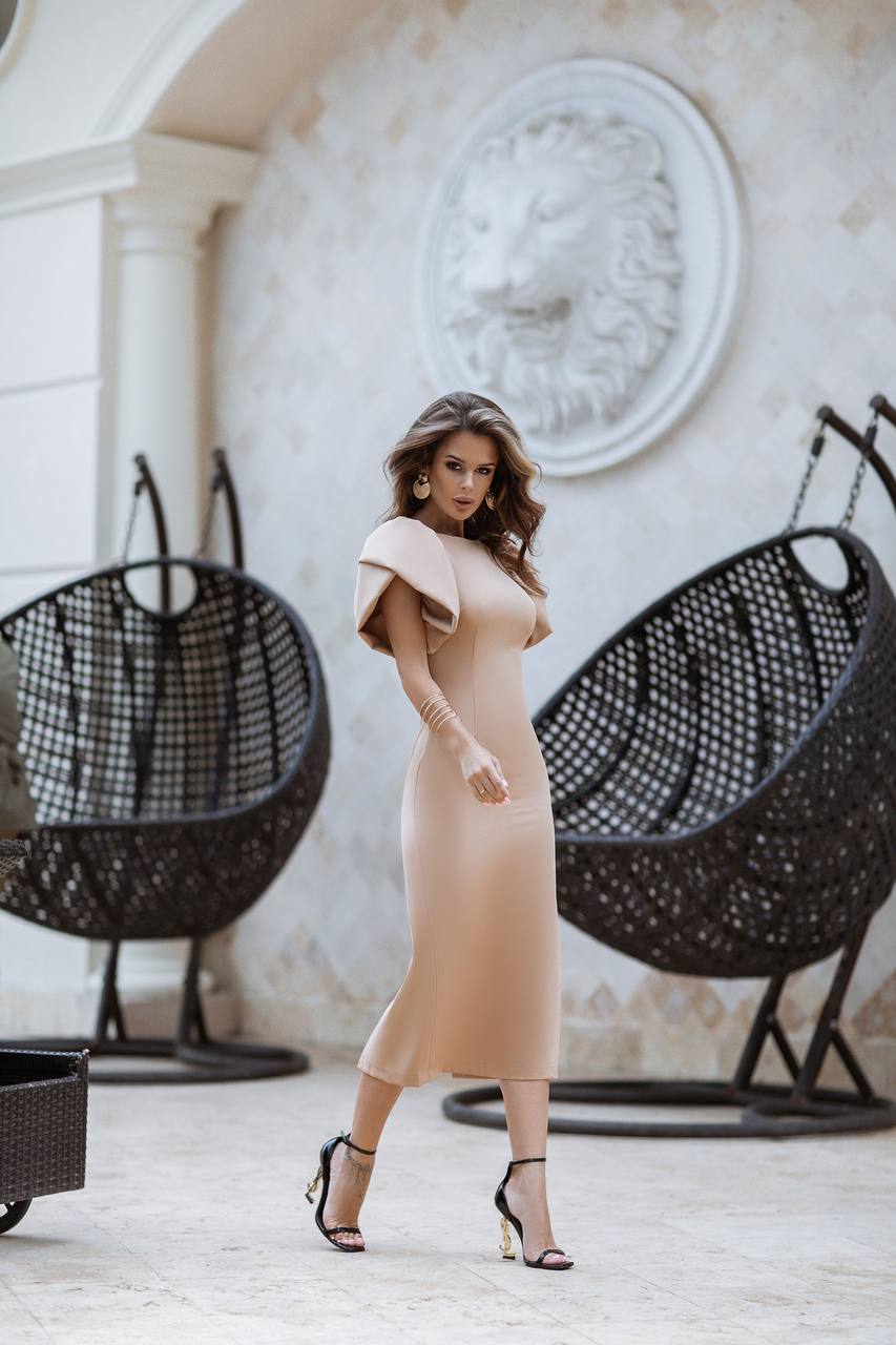 Woman in a beige dress standing in a stylish indoor setting with hanging chairs.