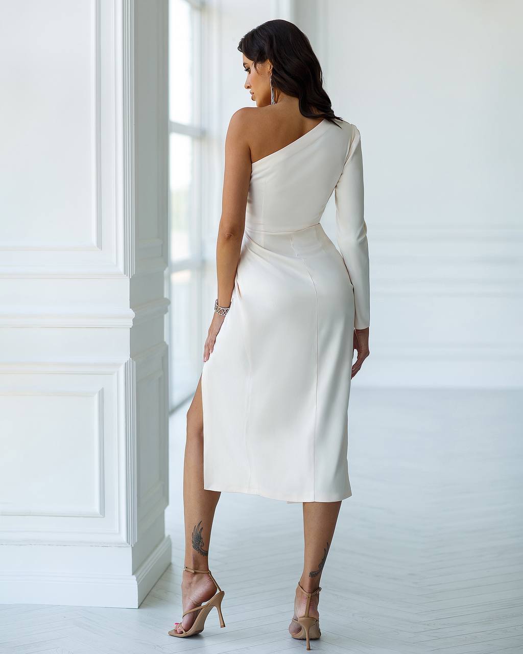 Woman wearing a white one-shoulder dress with a slit in a bright room.