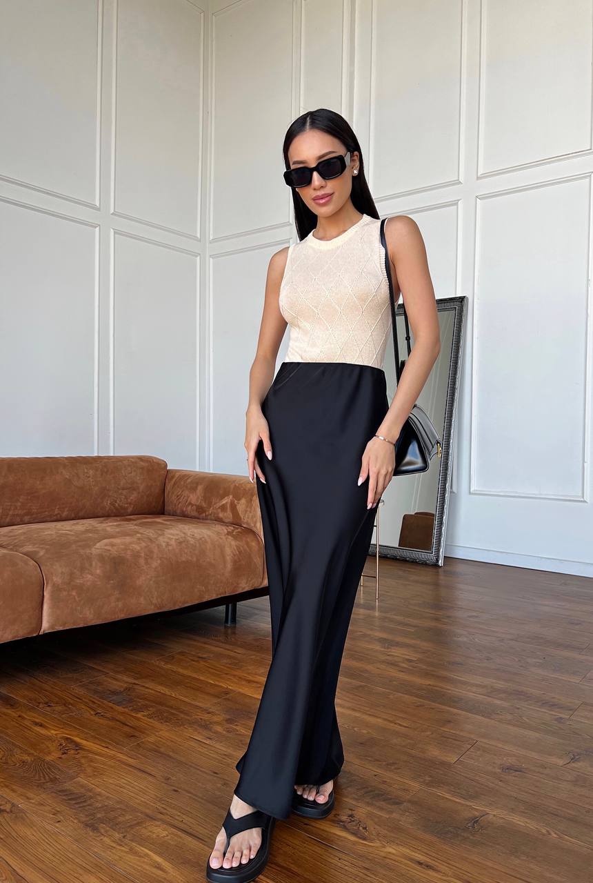Woman in a stylish outfit standing in a room with a brown sofa and white paneled walls.