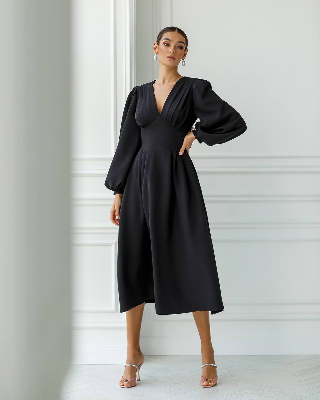 Woman wearing a black dress with long sleeves against a white wall