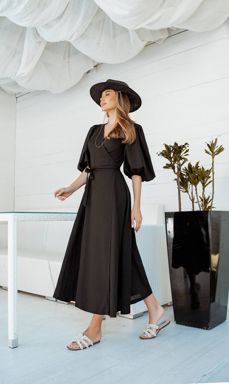 Woman in a black outfit standing in a modern interior setting with plants.