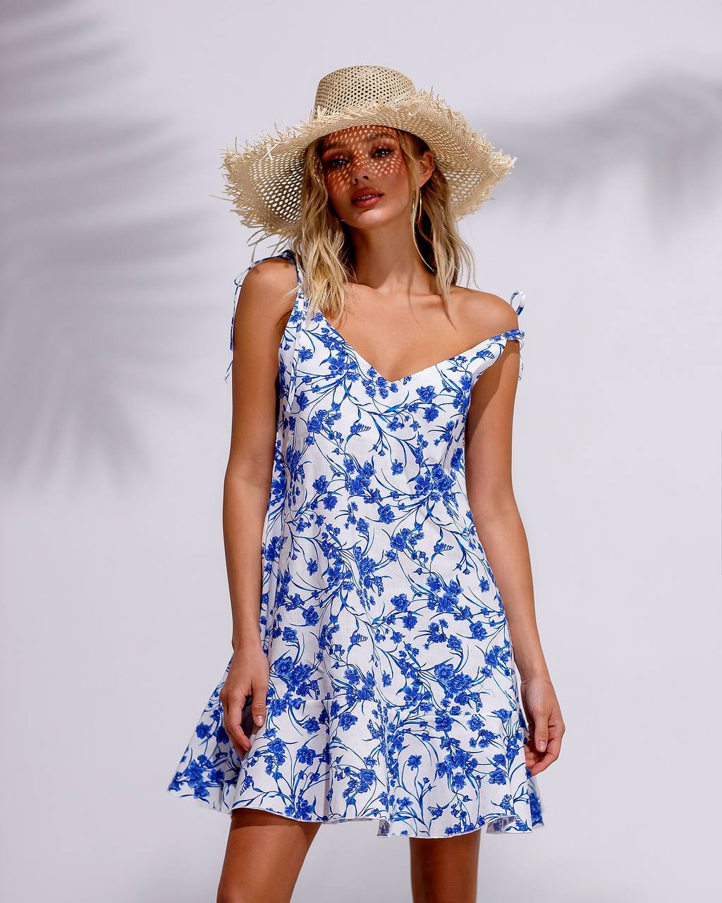 Woman wearing a blue floral dress and straw hat against a white background