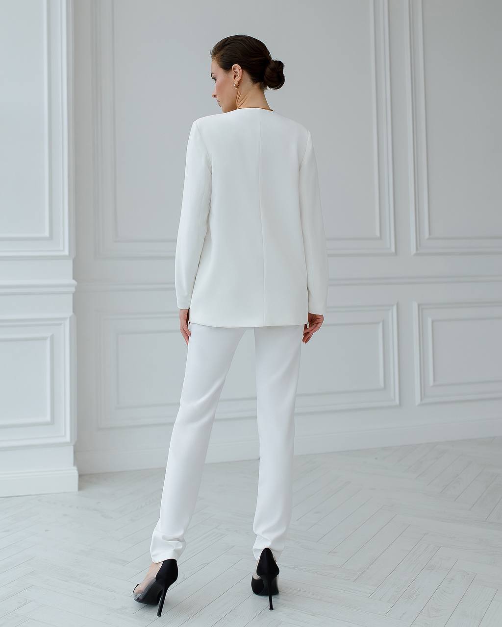 Woman wearing a white suit standing in a minimalistic room with white walls and floor.