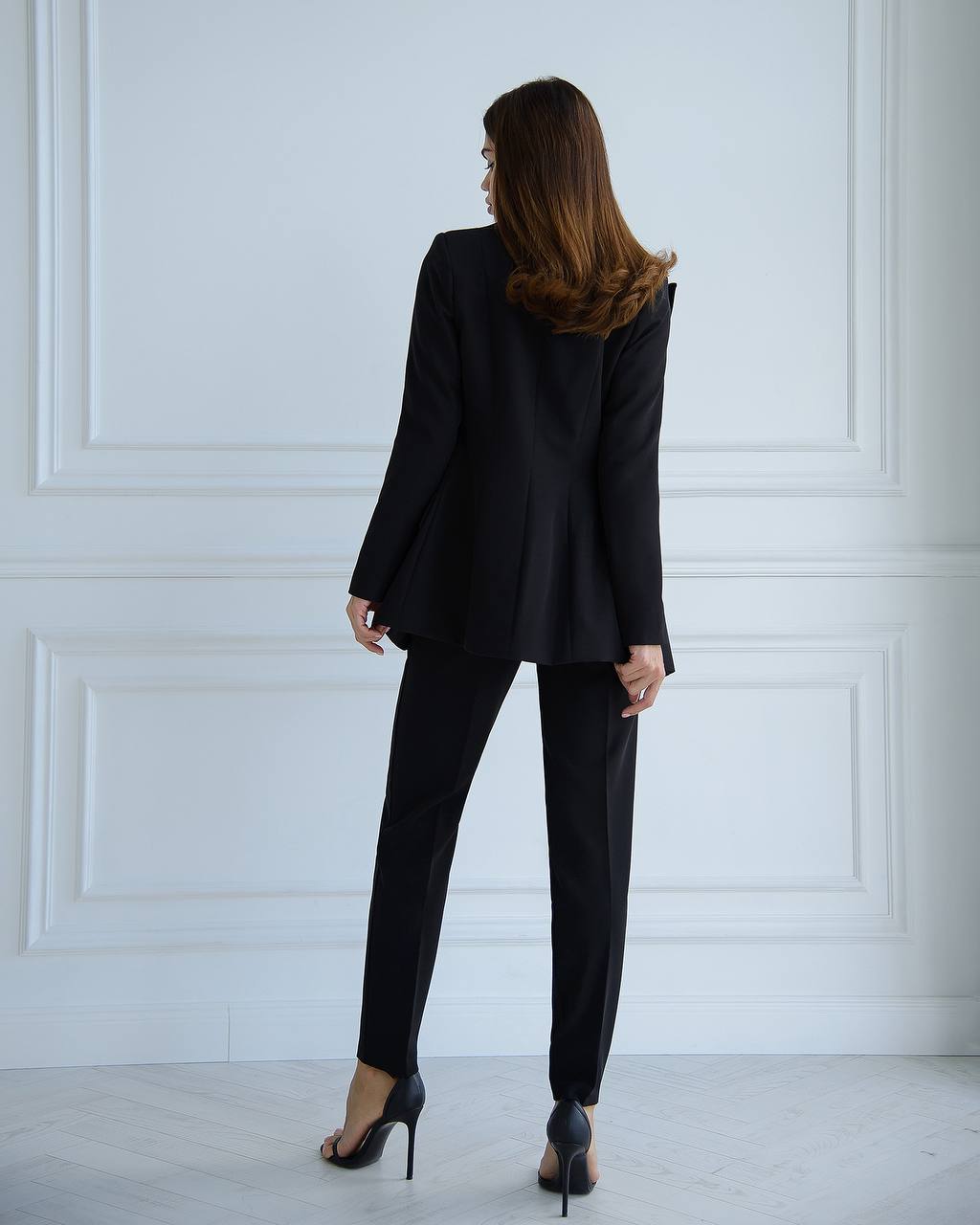 Woman wearing a black suit standing against a white paneled wall.