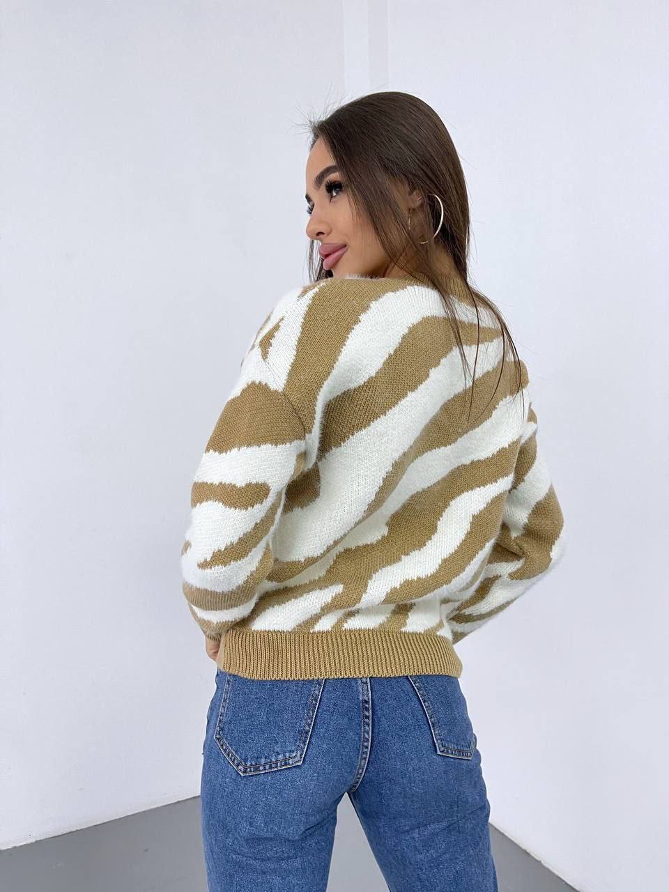 Woman wearing a brown and white striped sweater and blue jeans against a white background