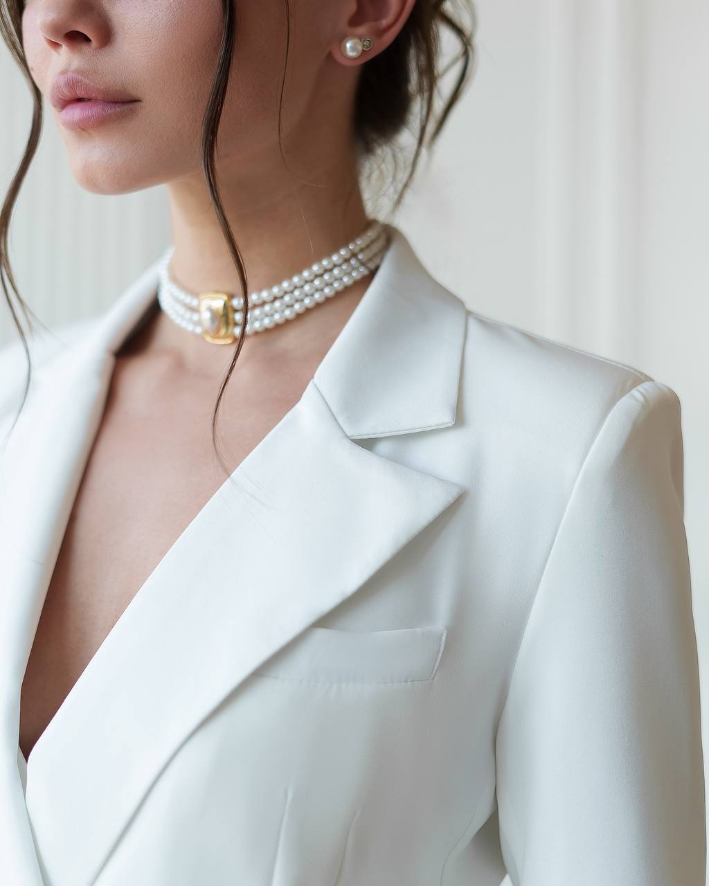 Close-up of a person wearing a white blazer and pearl necklace with a gold clasp.