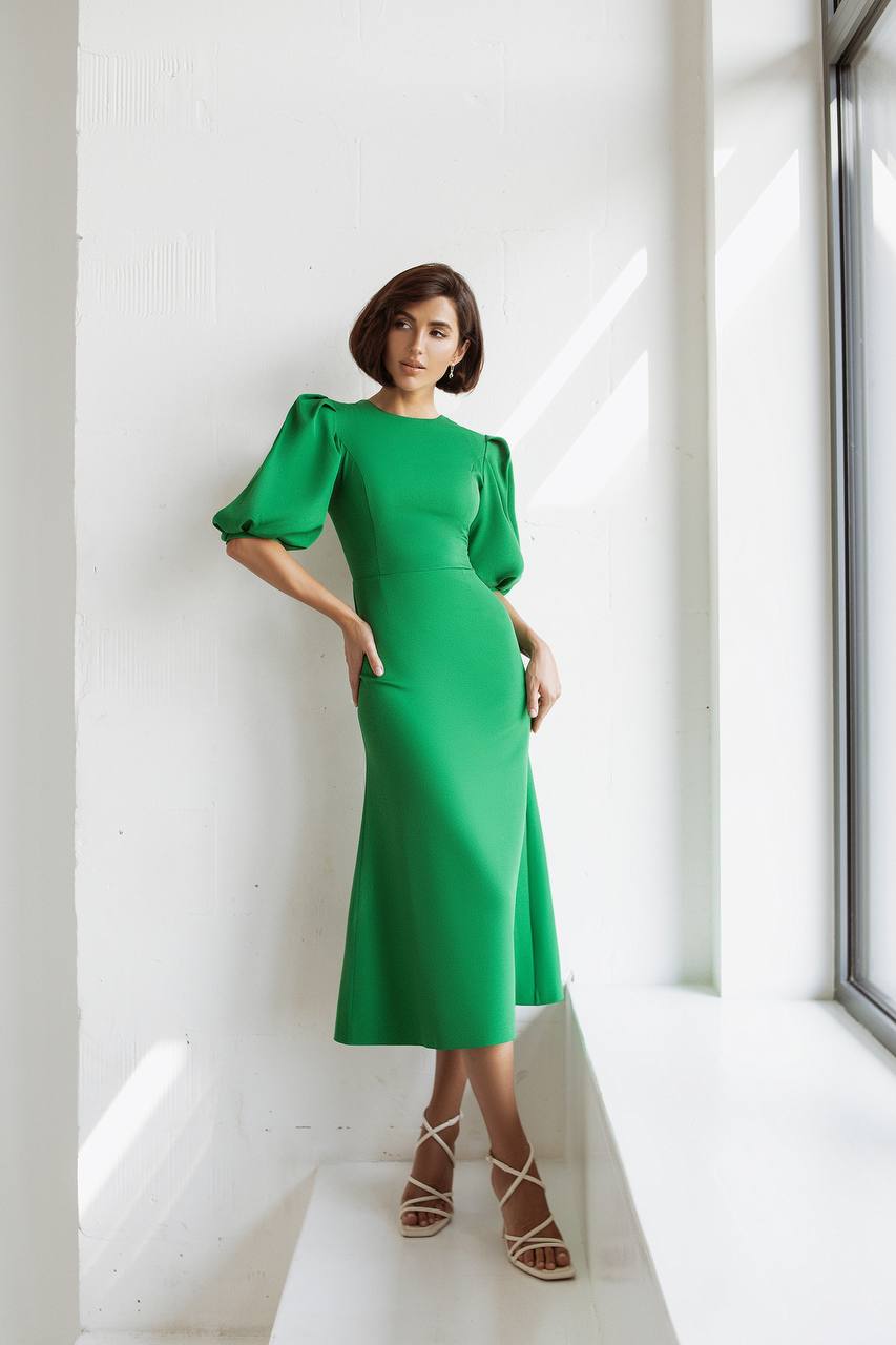 Woman wearing a green dress standing against a white wall.