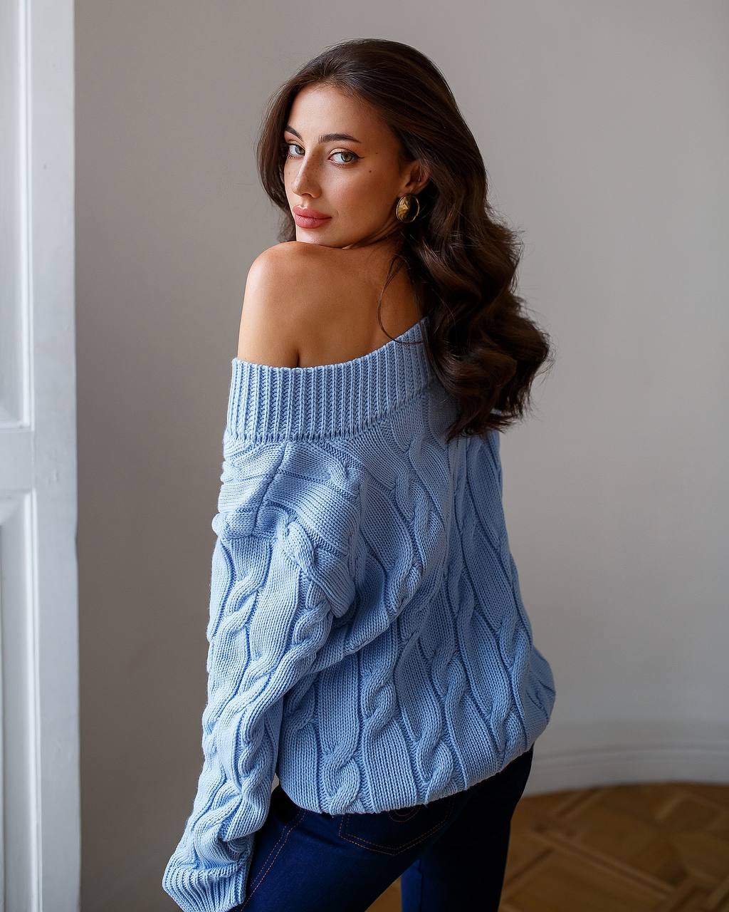 Woman wearing a light blue cable knit sweater against a neutral background