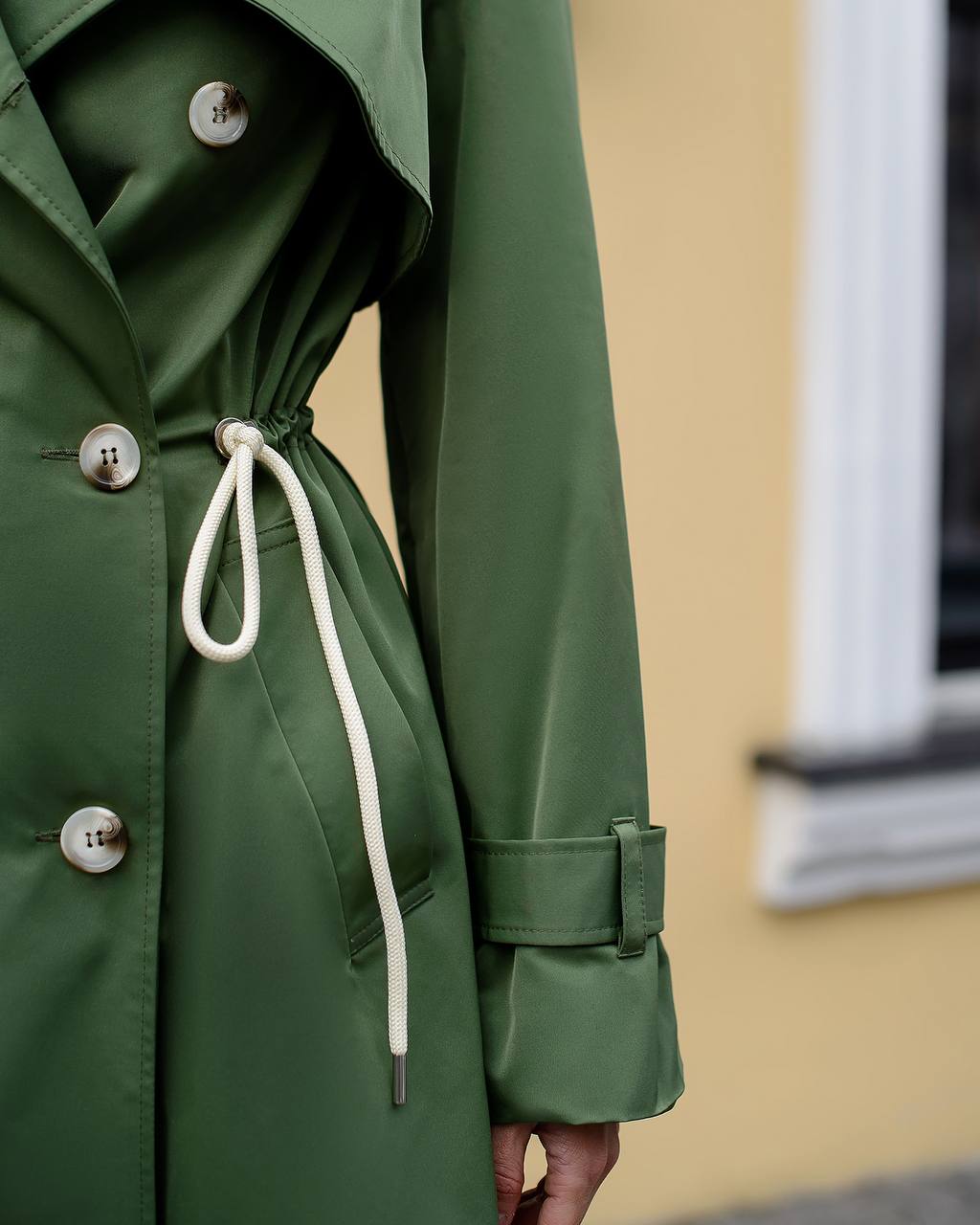 Green trench coat with buttons and drawstring on a neutral background