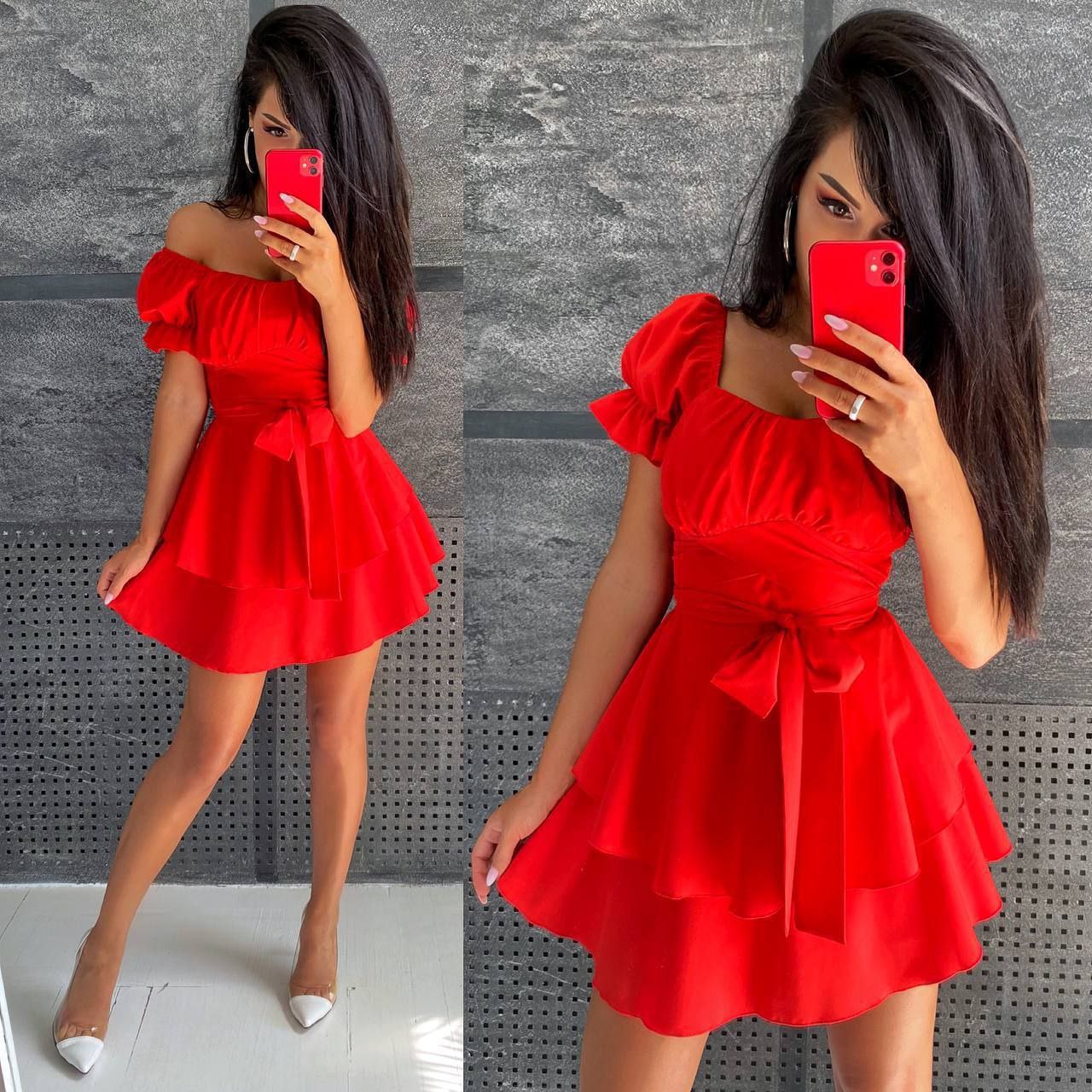 Woman wearing a red off-shoulder dress with a bow detail, taking a mirror selfie.