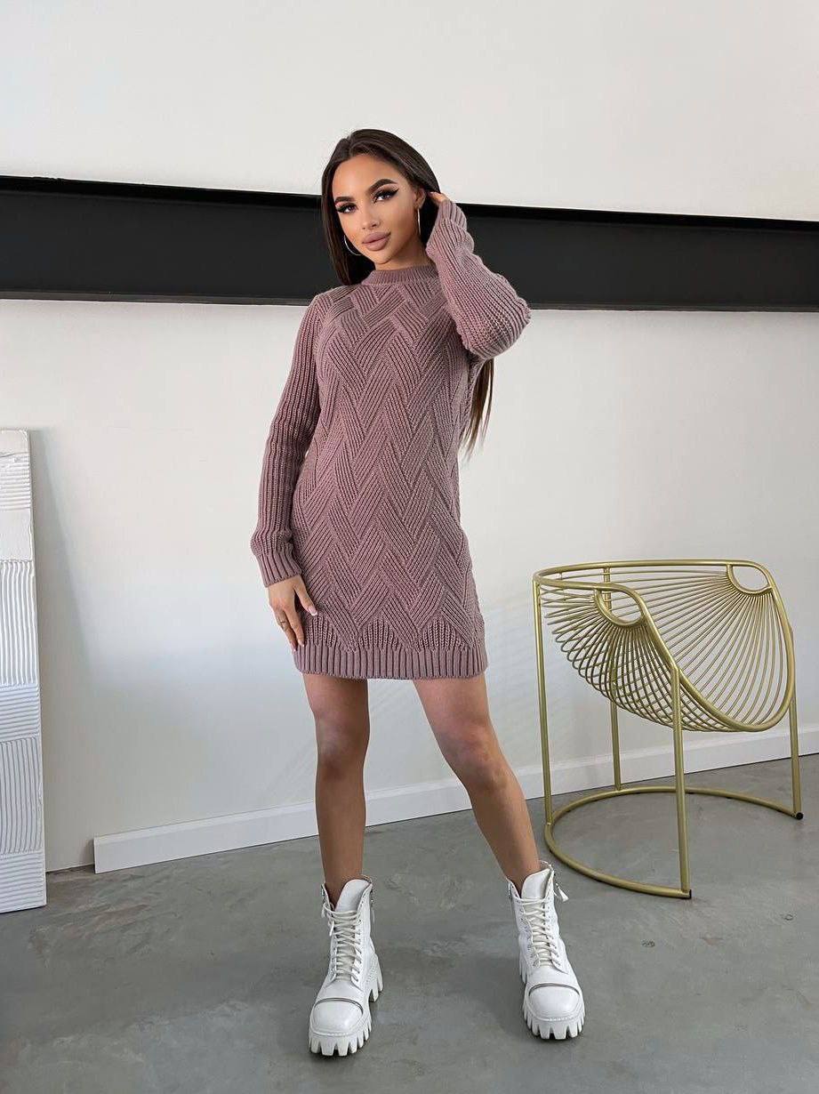 Woman wearing a pink knit dress and white sneakers in a minimalistic room.