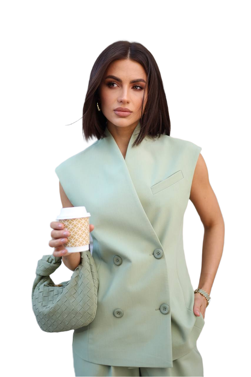 Woman wearing a light green sleeveless blazer holding a coffee cup on a white background