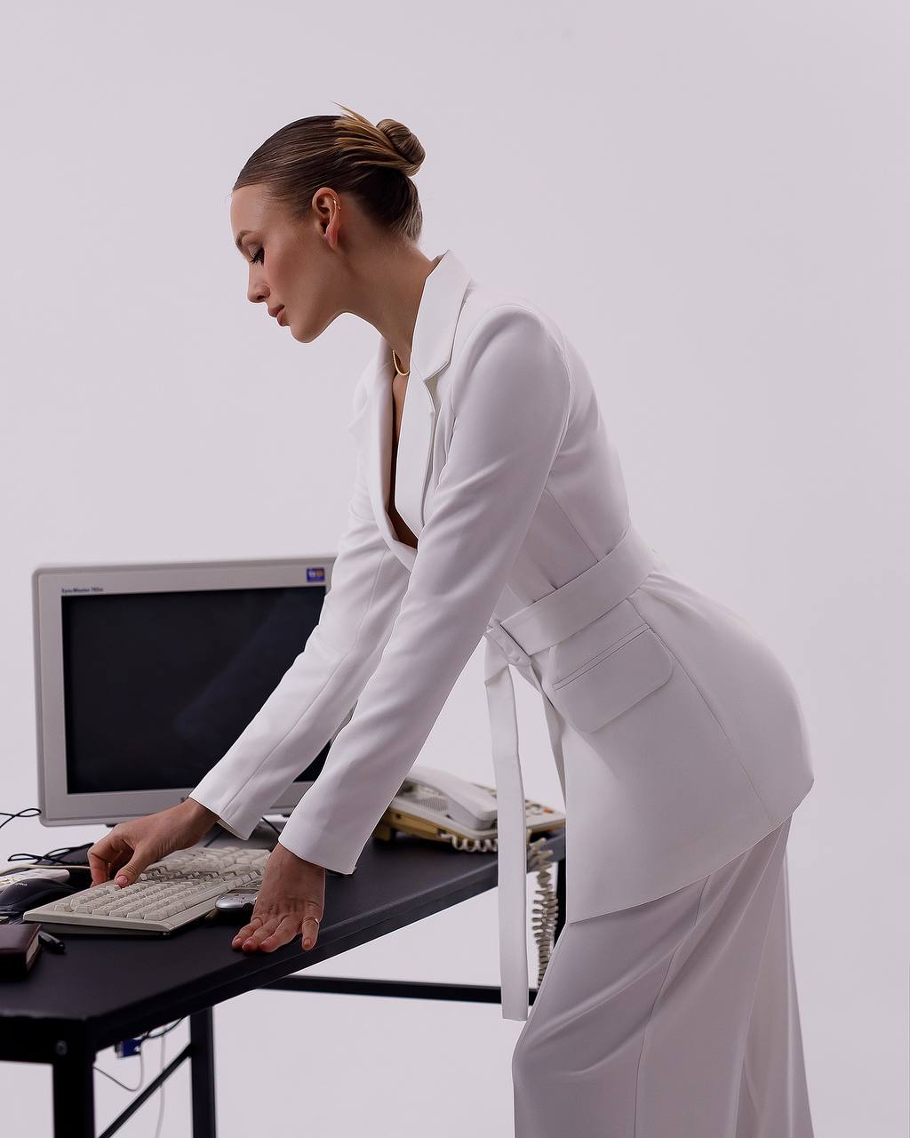 Woman in a white outfit using a computer on a desk against a plain background