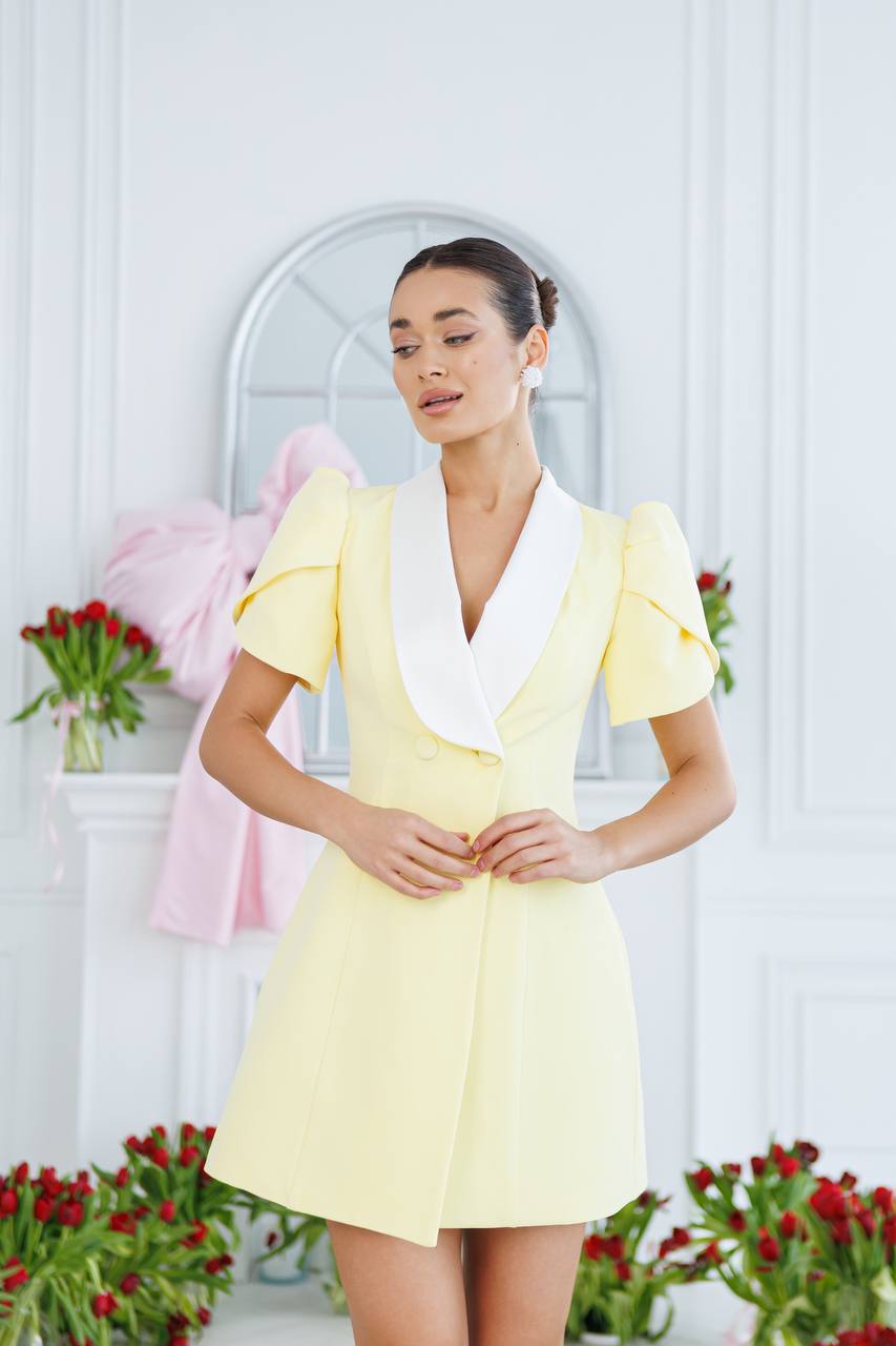 Woman in a yellow dress standing in front of a mirror with flowers around.