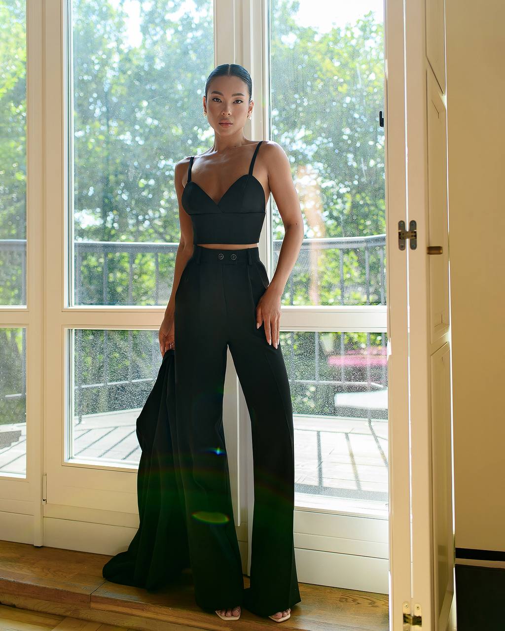 Woman in a black outfit standing in a room with large windows.