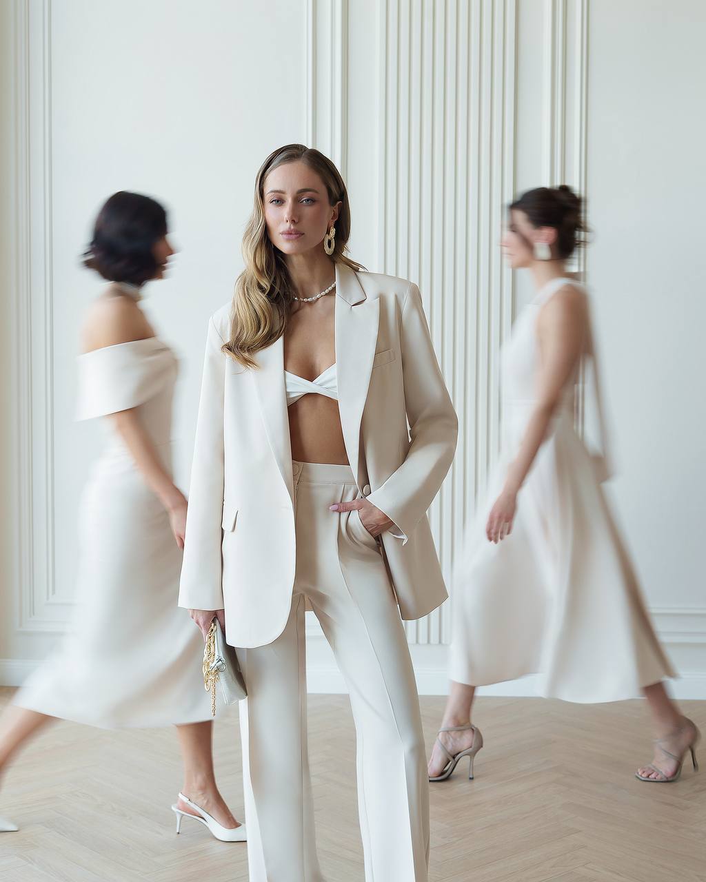 Woman in a white suit standing in a room with mirrors reflecting her image.