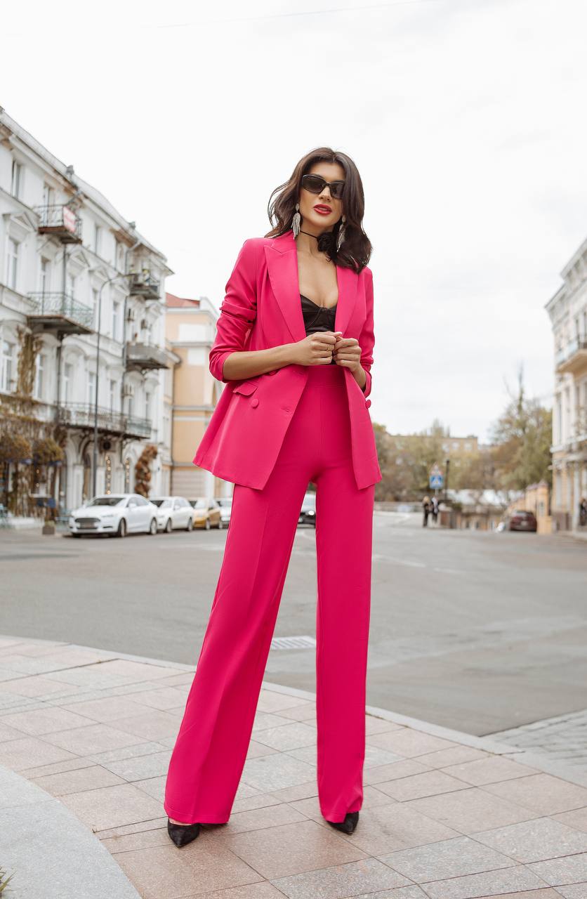 Woman in a bright pink suit standing on a city street.