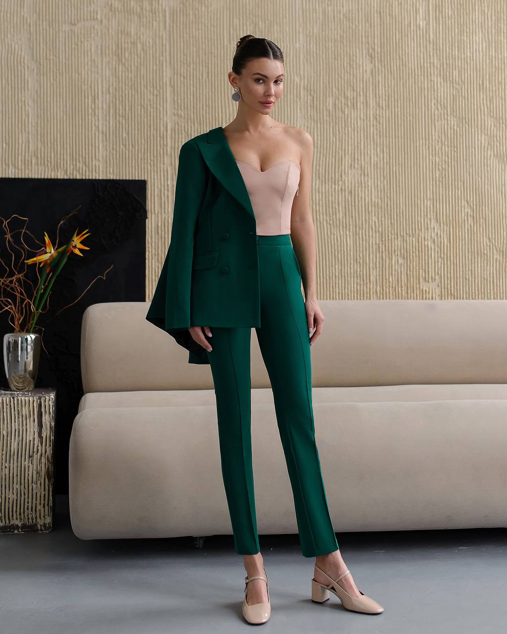 Woman in a green suit standing in a room with a beige sofa and decorative elements.