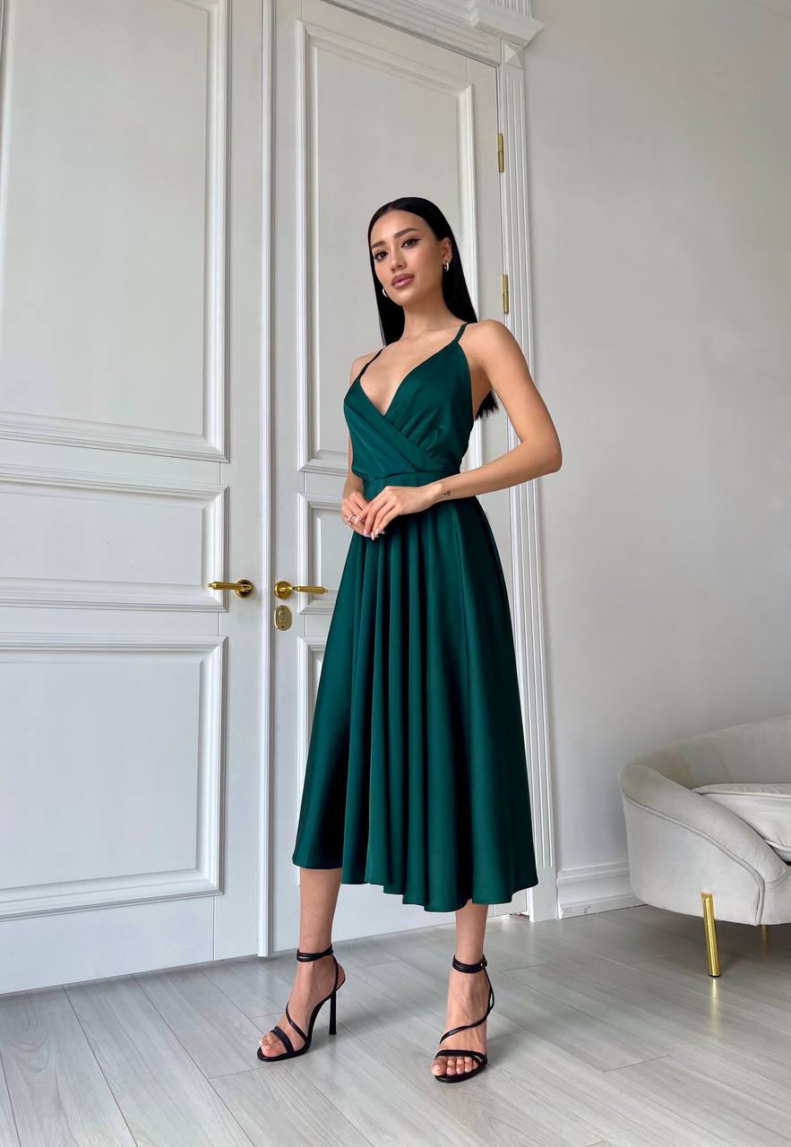 Woman in a green dress standing in a room with white walls and a white door.