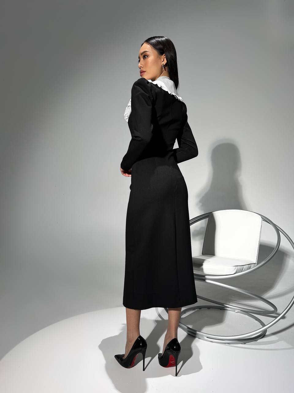 Woman in a black dress with white collar standing in a minimalistic setting.