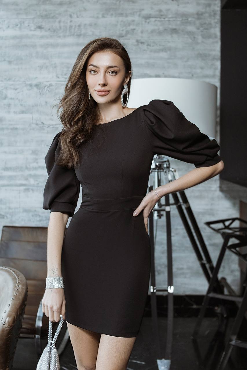 Woman in a black dress posing indoors with a neutral background