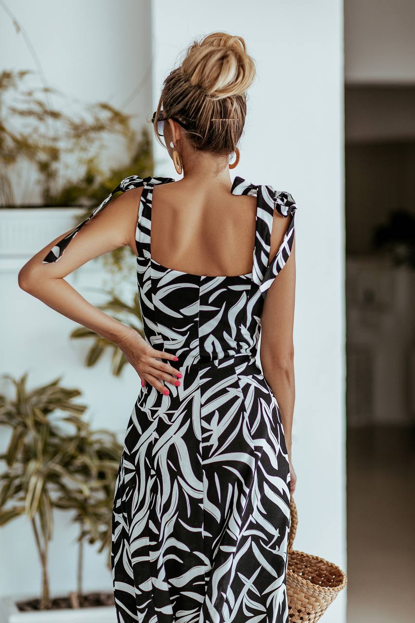 Woman wearing a black and white patterned dress in an indoor setting with plants.