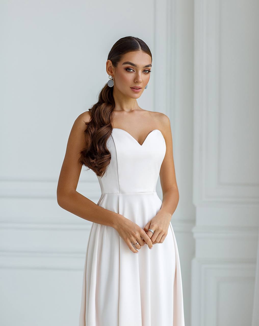 Woman wearing a white strapless dress against a plain background
