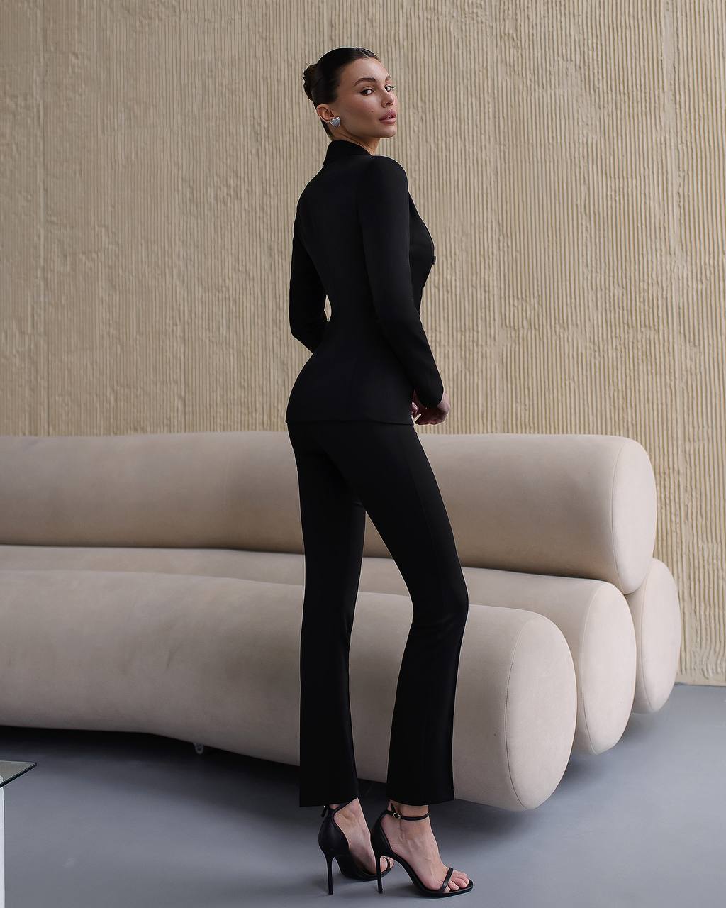 Woman in a black outfit standing in a modern interior setting with beige sofa and wall.