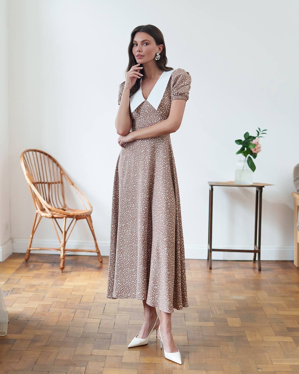 Woman in a patterned dress standing in a room with wooden flooring and minimal decor.