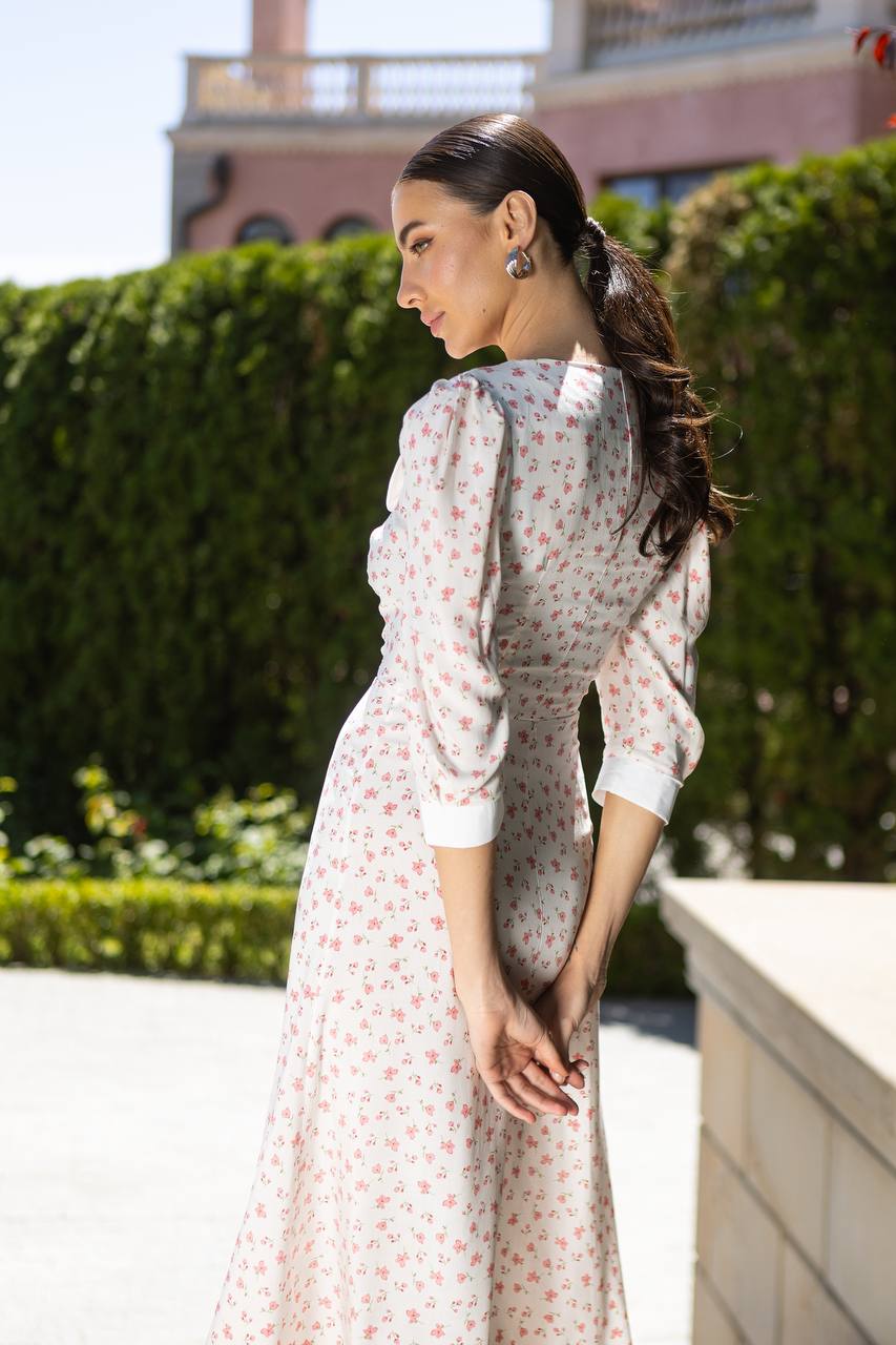 Woman in a floral dress standing outdoors with greenery in the background