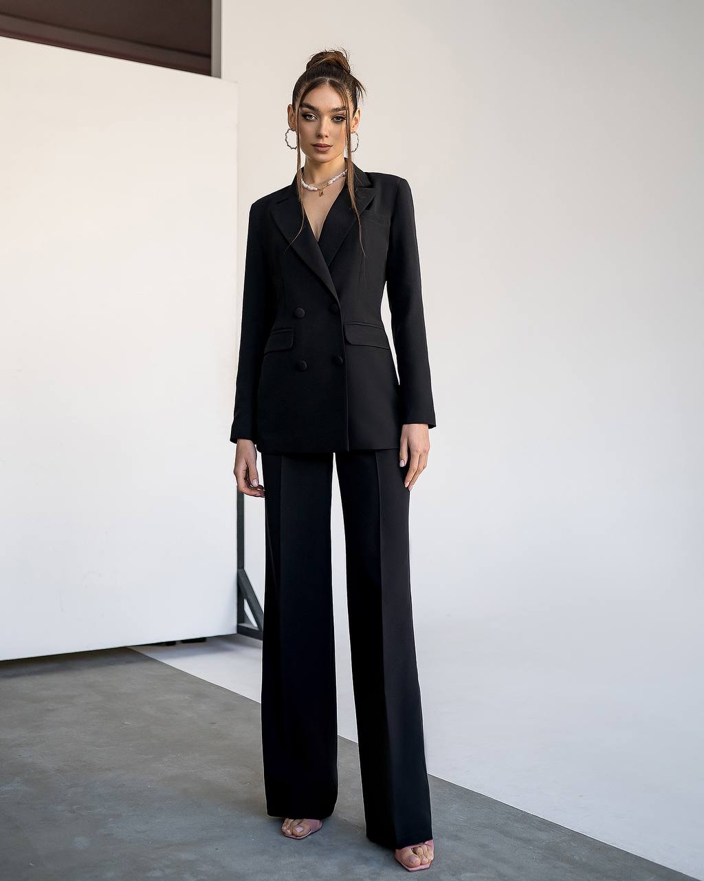 Woman wearing a black suit standing against a white wall.