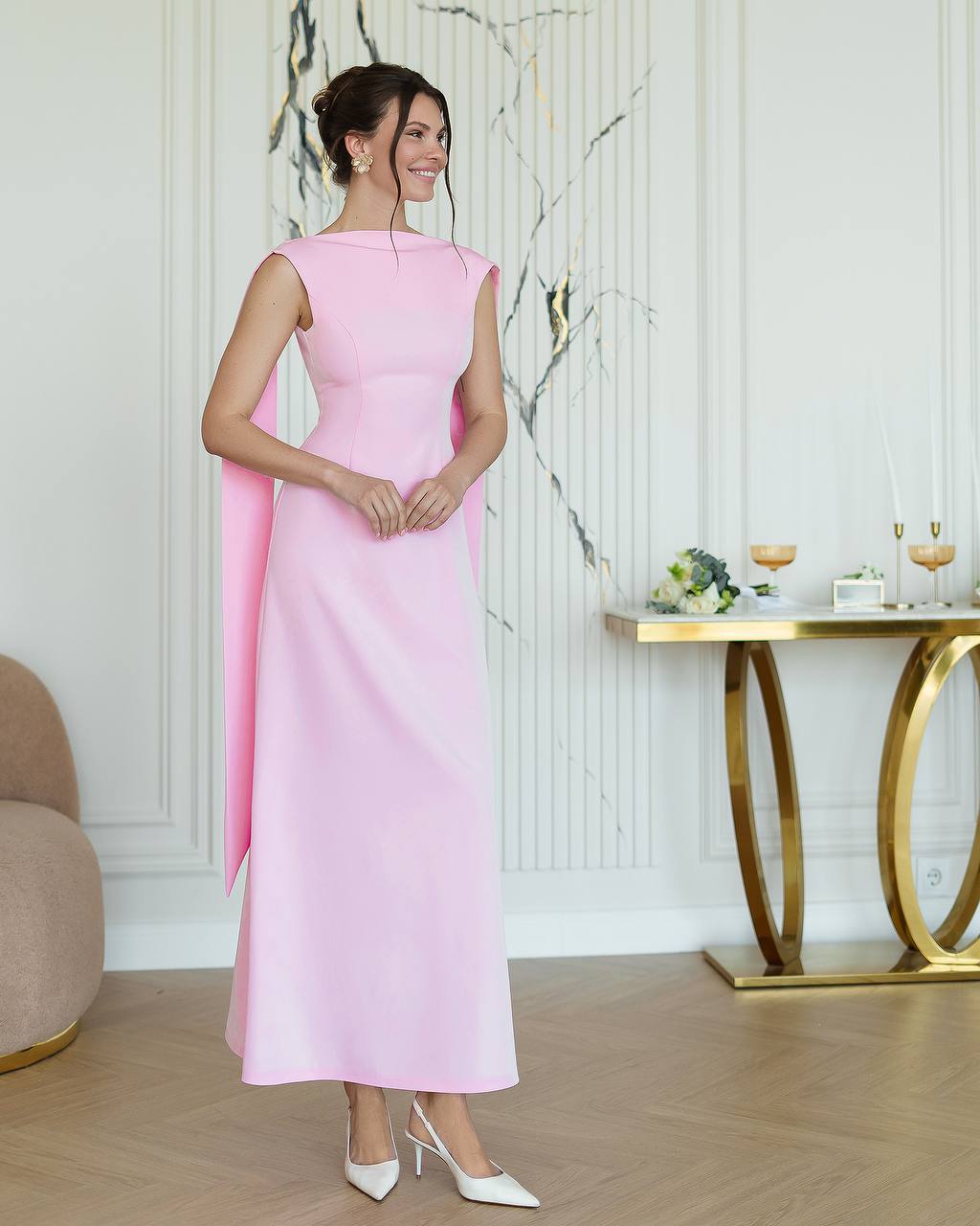 Woman in a pink dress standing in an elegant room with a marble wall and gold table.