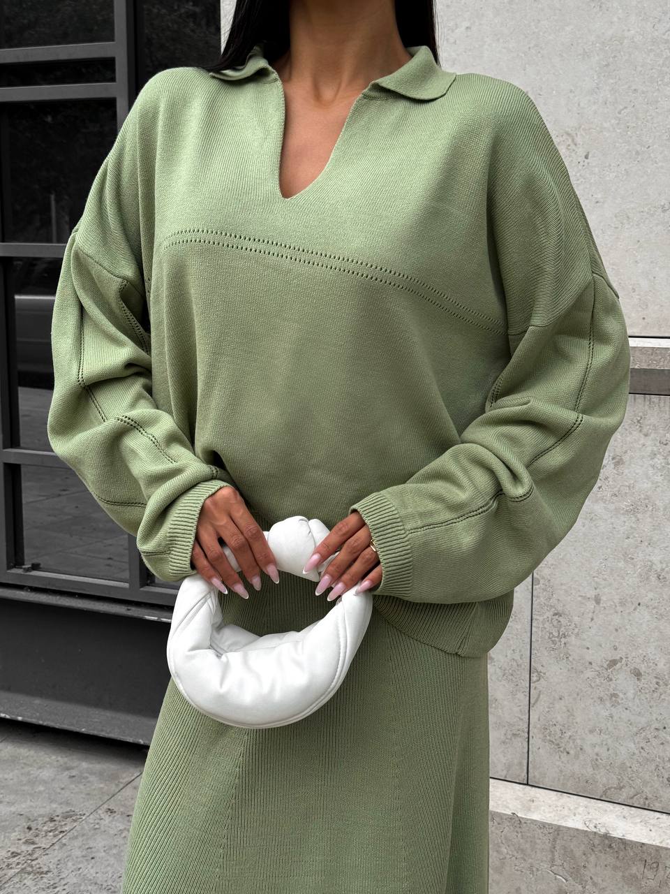 Person wearing a green dress holding a white cushion against a concrete wall.