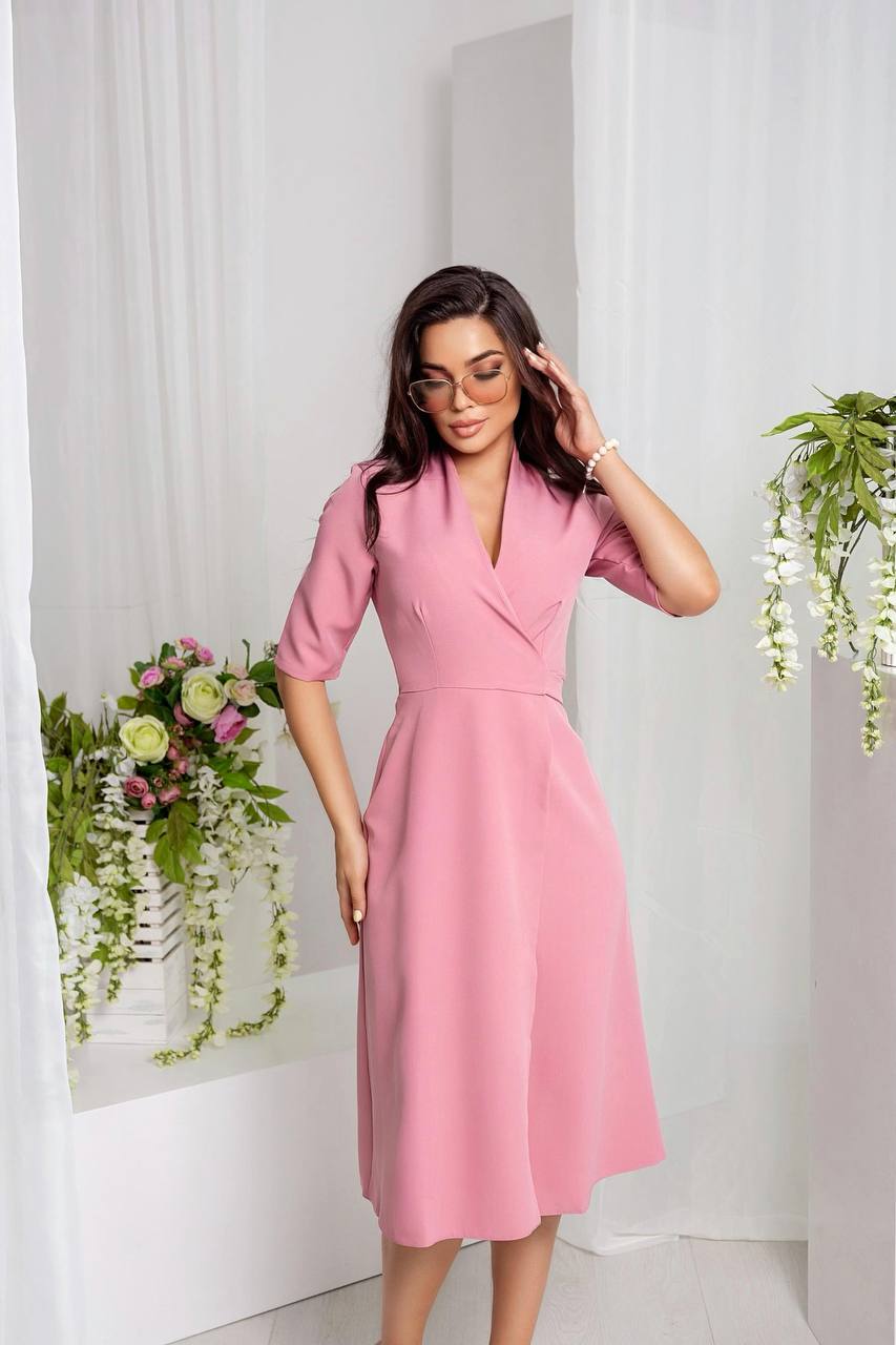 Woman wearing a pink dress in a minimalistic setting with plants and flowers.